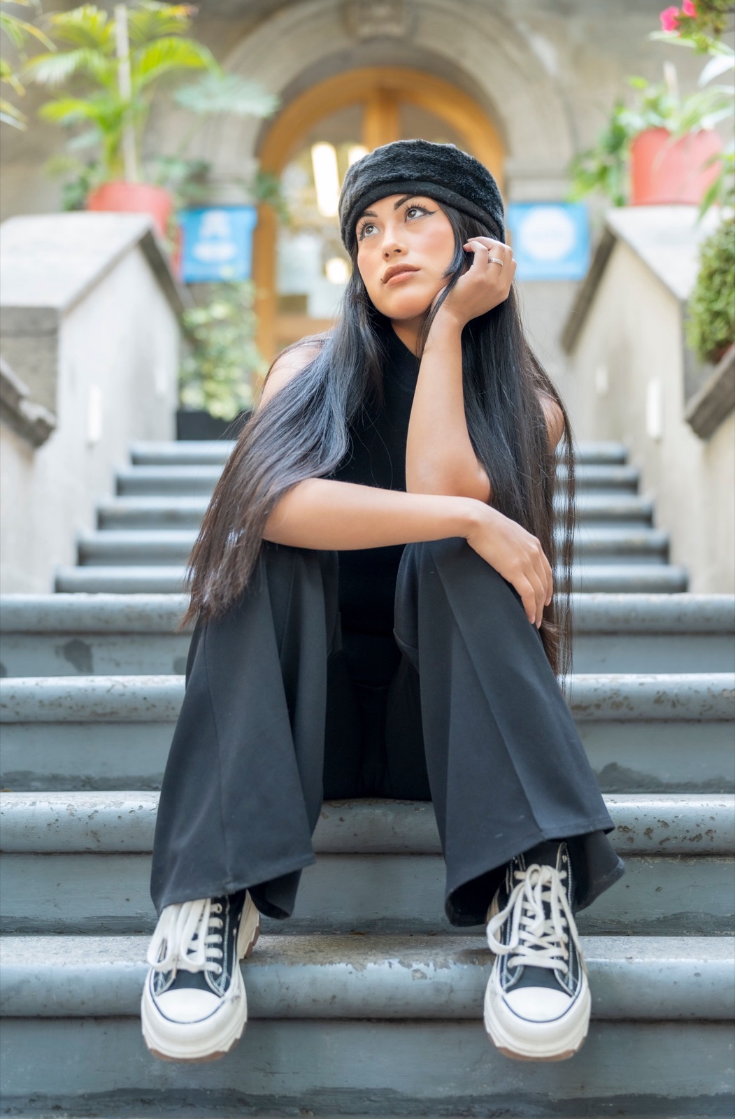 Woman in wide-leg trousers and sneakers seated on stone steps.